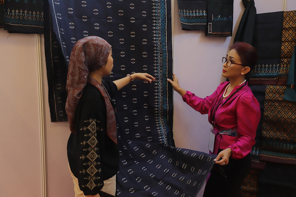A visitor speaks with a Cham Silk weaver at the SheTrades Exhibition. DC-Cam